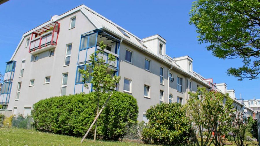 Modernes Wohngebäude mit grüner Umgebung und klarer Himmel im Hintergrund.