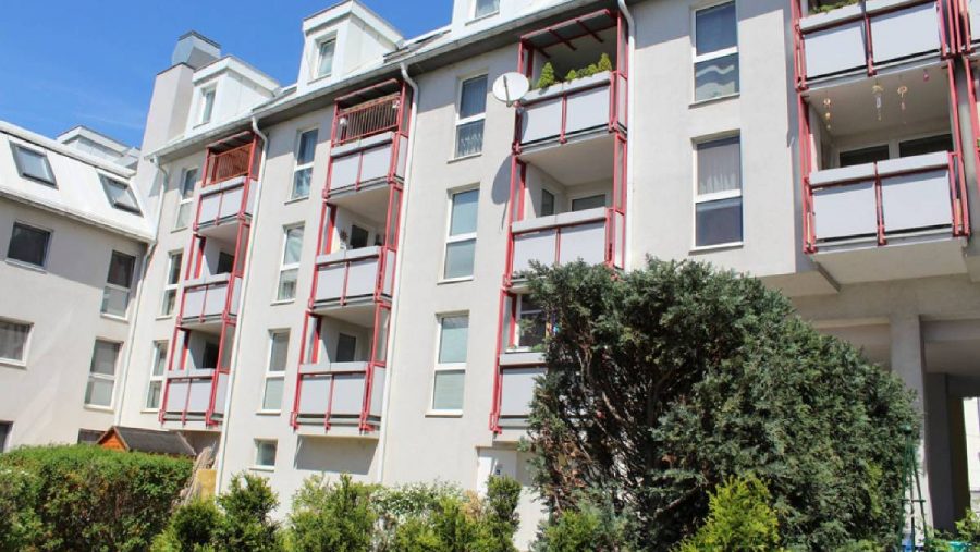 Mehrfamilienhaus mit Balkonen und Gartenansicht bei sonnigem Wetter.