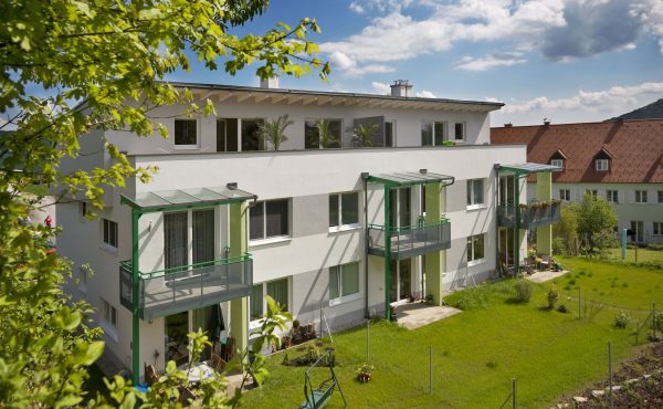 Moderne Wohngebäude mit Balkonen und Garten im Sommer bei sonnigem Wetter und blauem Himmel.