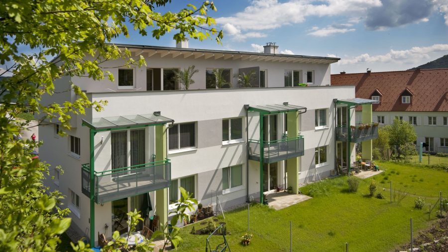 Moderne Wohngebäude mit Balkonen und Garten im Sommer bei sonnigem Wetter und blauem Himmel.