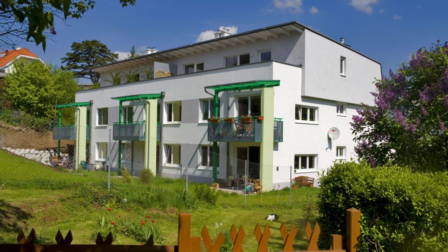 Modernes Wohngebäude mit Garten, bunten Blumen und blauem Himmel im Hintergrund.