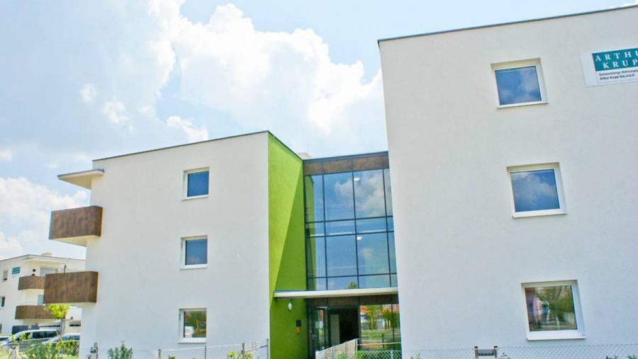 Moderne Wohngebäude aus weißem und grünem Putz mit Glasfassade und blauen Himmel im Hintergrund.