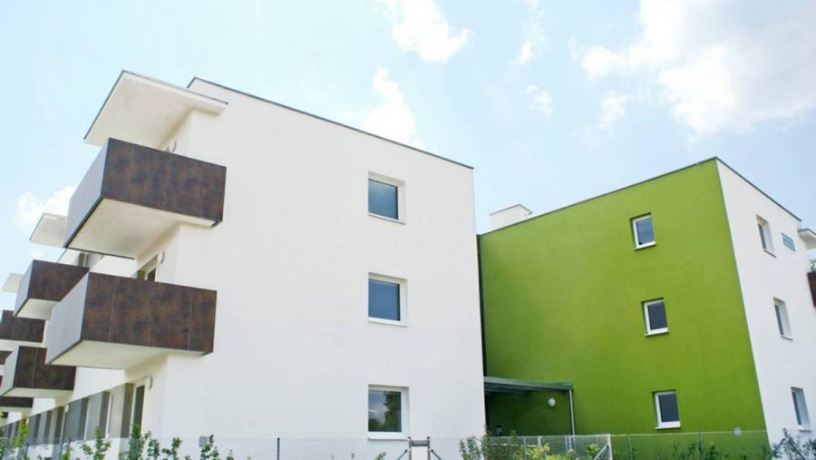 Moderne Wohngebäude mit weißen und grünen Fassaden unter blauem Himmel.