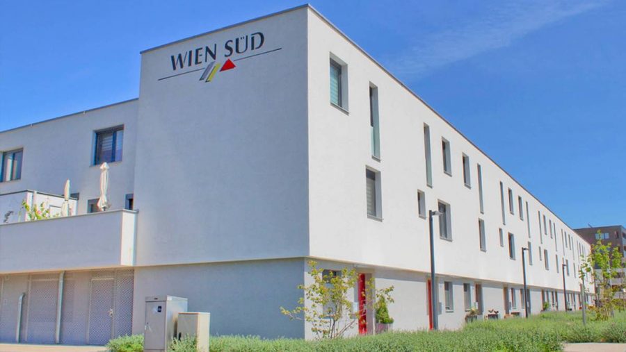 Moderne Wohnanlage mit weißer Fassade unter blauem Himmel, grüner Umgebung im Vordergrund.