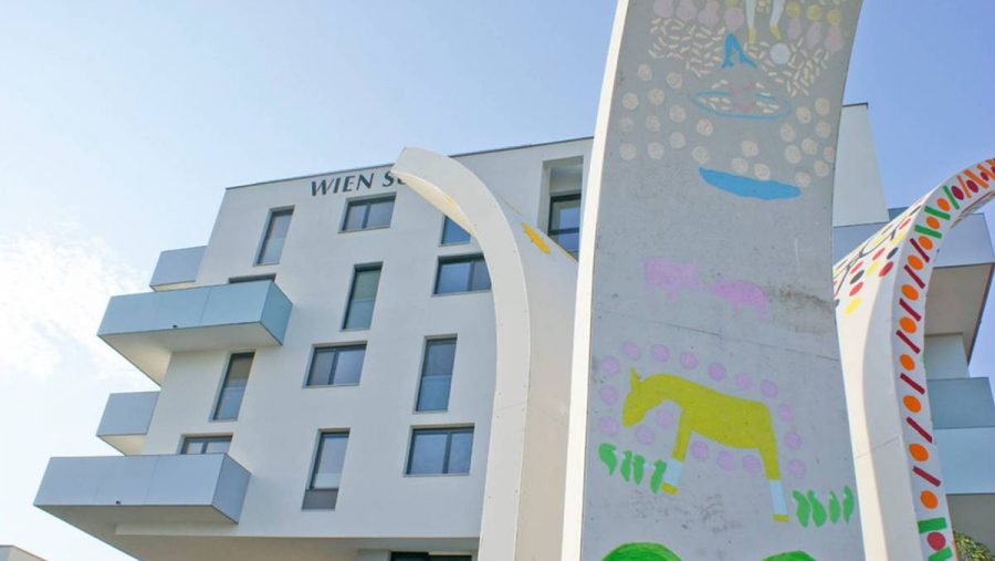 Moderne Architektur mit farbenfrohen Kunstwerken an einem Gebäude, sommerlicher Himmel im Hintergrund.