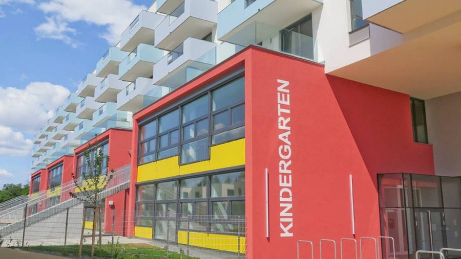 Moderne Kindergartengebäude mit roter und gelber Fassade unter blauem Himmel.