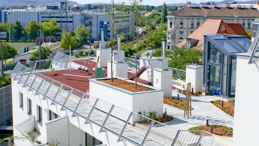 Moderne Dachlandschaft mit Belüftung und begrüntem Bereich in einer städtischen Umgebung.