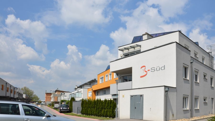 Moderne Stadthäuser an einem sonnigen Tag mit Autos auf der Straße, blauer Himmel im Hintergrund.