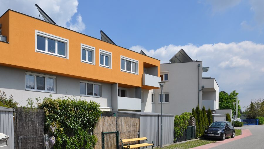 Moderne Wohnhäuser mit Solarpaneelen und orangener Fassade an einem sonnigen Tag.