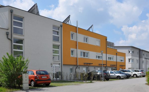 Moderne Reihenhäuser mit geparkten Autos an sonnigem Tag.