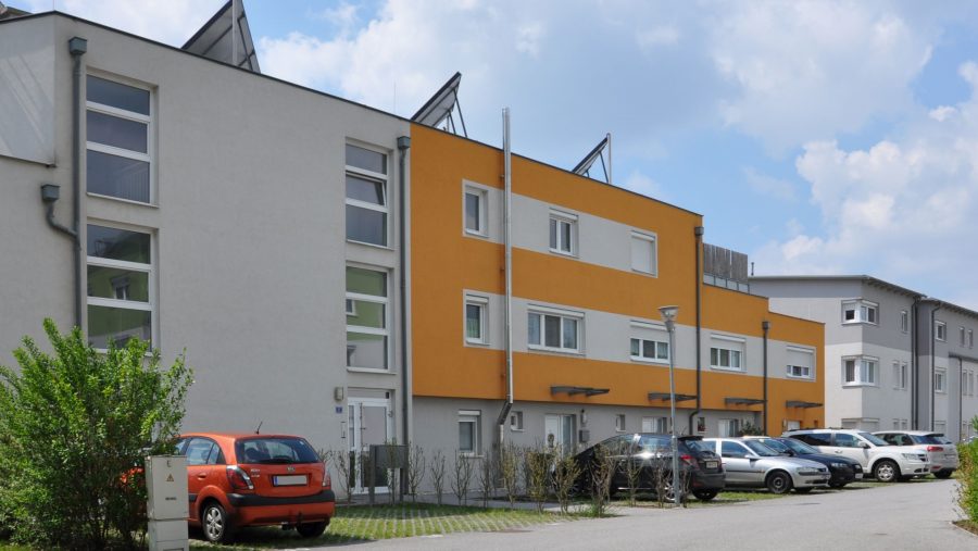 Moderne Reihenhäuser mit geparkten Autos an sonnigem Tag.