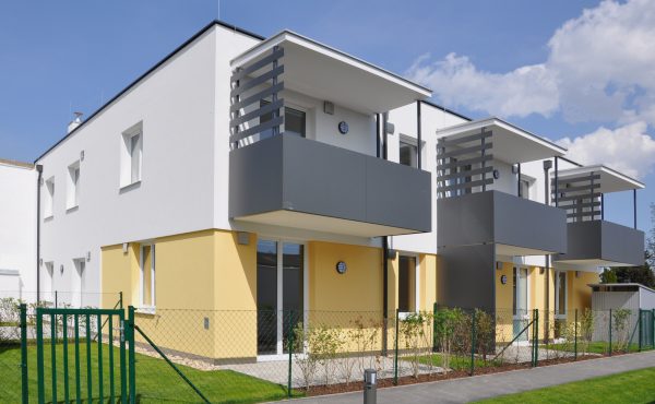 Moderne Reihenhäuser mit Balkonen und Garten bei sonnigem Wetter.