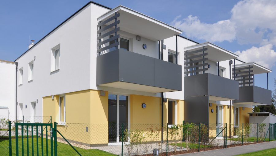 Moderne Reihenhäuser mit Balkonen und Garten bei sonnigem Wetter.