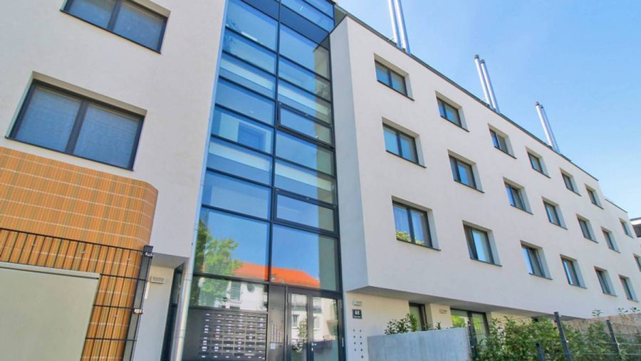 Moderne Fassade eines mehrstöckigen Bürogebäudes mit Glas- und Betonelementen bei sonnigem Himmel.