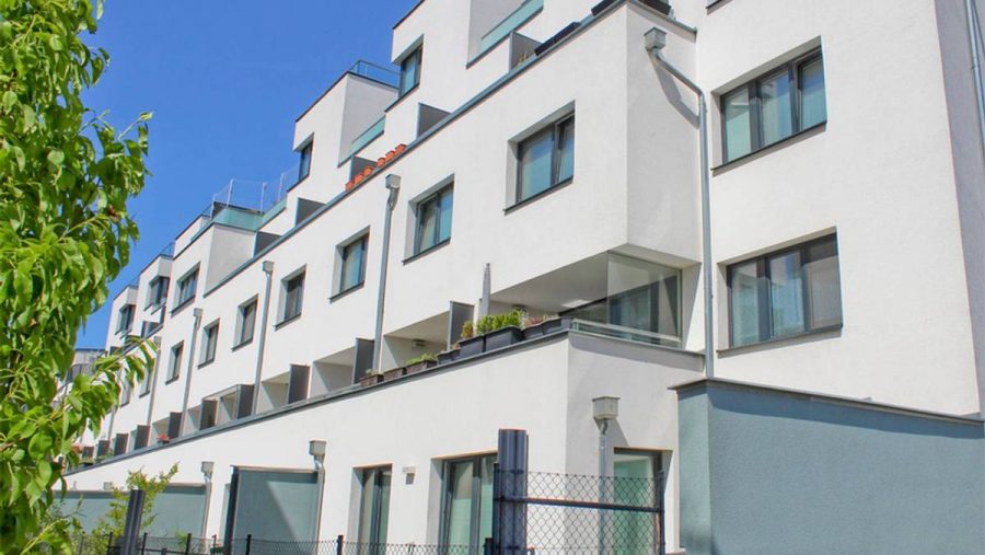 Moderne Wohngebäude mit Balkonen und blauer Fassade an einem sonnigen Tag.