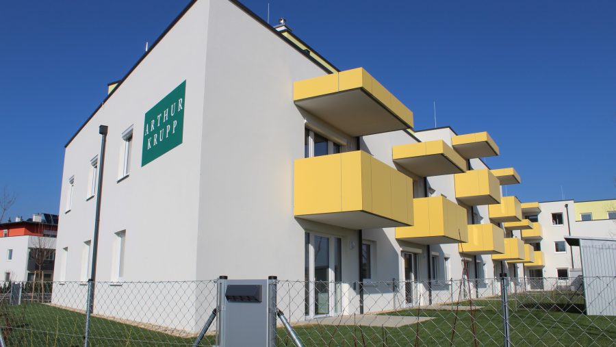 Modernes Wohngebäude mit gelben Balkonen und blauem Himmel im Hintergrund.