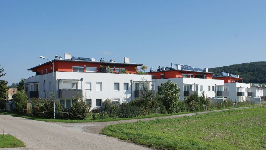 Moderne Wohnanlage mit Solarpanelen und Garten vor einem Wald.