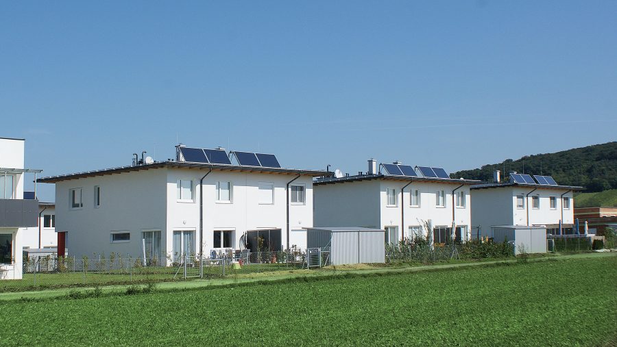 Reihenhäuser mit Solaranlagen auf den Dächern in einer grünen Umgebung.
