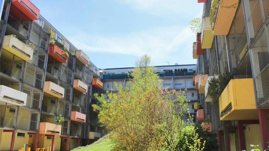 Moderne Wohnanlage mit bunten Balkonen und Garten, sonniger Himmel im Hintergrund.