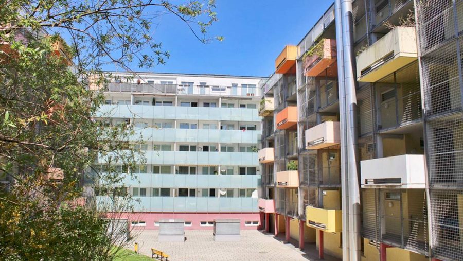 Mehrstöckiges Wohngebäude mit Balkonen und Innenhof, sonniger Tag.