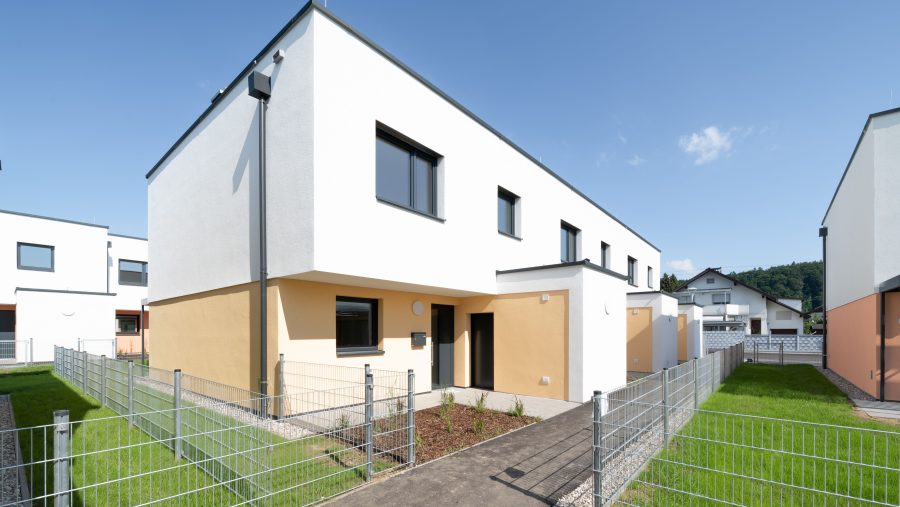 Moderne Reihenhäuser mit Garten und Zaun bei sonnigem Wetter.