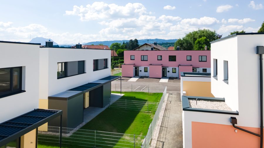 Moderne Stadthäuser mit bunten Fassaden, blauer Himmel und grüne Umgebung im Hintergrund.