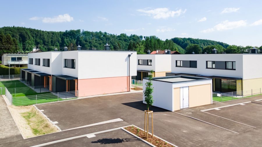 Moderne Reihenhäuser mit Terrassen in einer grünen Umgebung bei sonnigem Wetter.