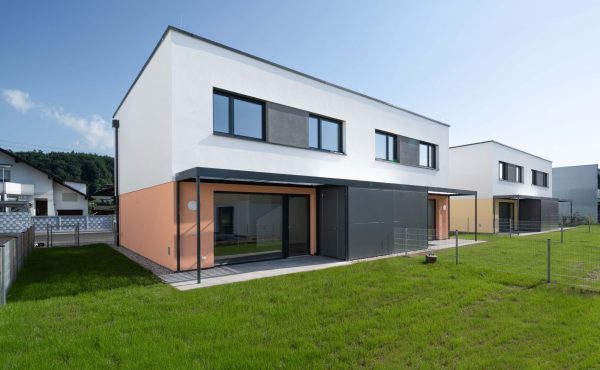 Zwei moderne Doppelhaushälften mit Garten und blauem Himmel im Hintergrund.