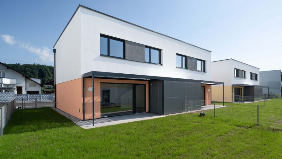 Zwei moderne Doppelhaushälften mit Garten und blauem Himmel im Hintergrund.
