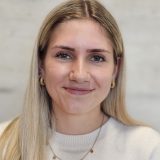 Porträt einer lächelnden Frau mit langem blondem Haar in weißem Pullover.