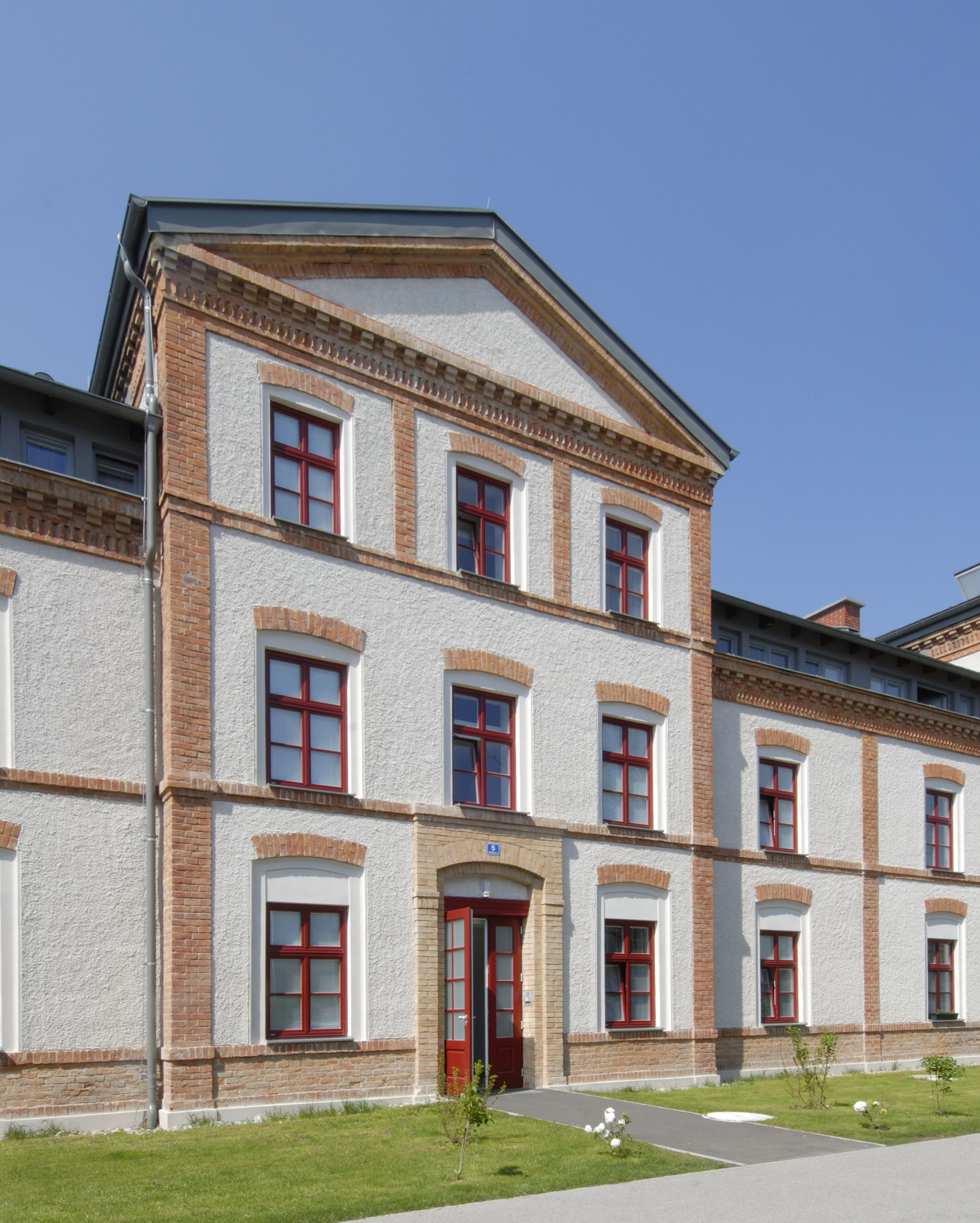 Referenz Felixdorf Historisches Gebäude mit roter Backsteinarchitektur und weißen Wänden, blauer Himmel im Hintergrund.