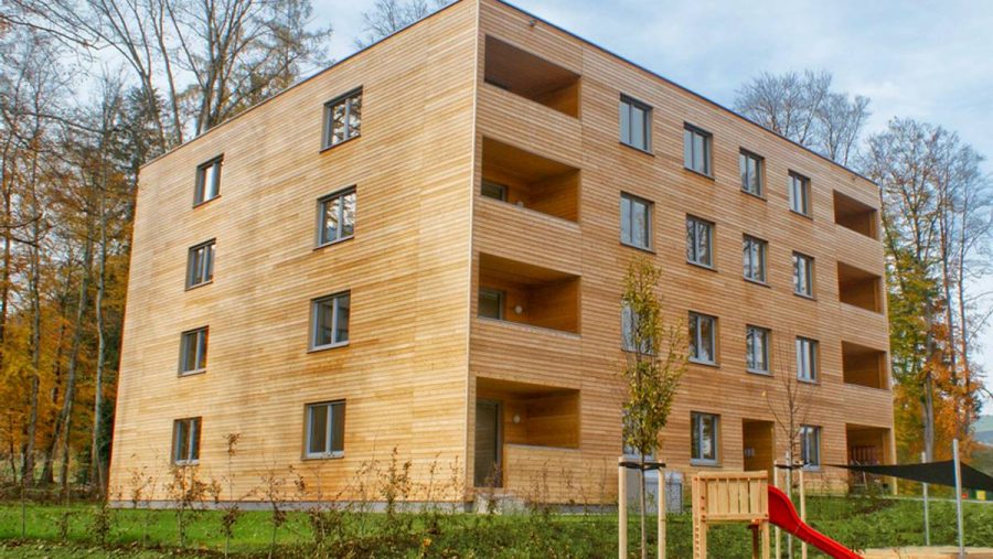 Mehrstöckiges Holzgebäude im Freien mit grüner Umgebung und kleinem Spielplatz im Vordergrund.