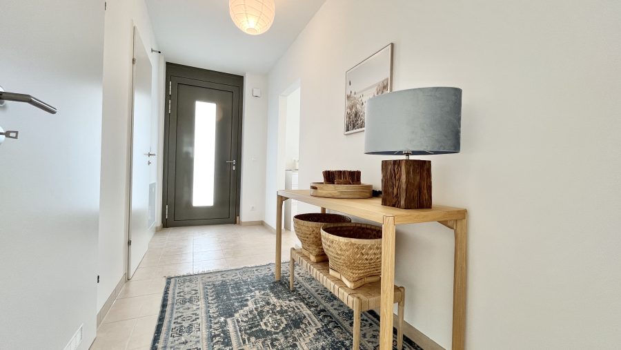 Moderner Eingangsbereich mit Holzkonsole, Lampe und Textilteppich vor einer Haustür.