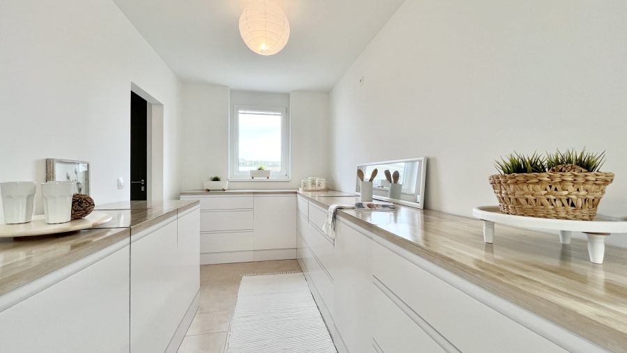 Moderne, minimalistische Küche mit weißen Schränken und Holzarbeitsplatten, dekoriert mit Pflanzen und Geschirr.