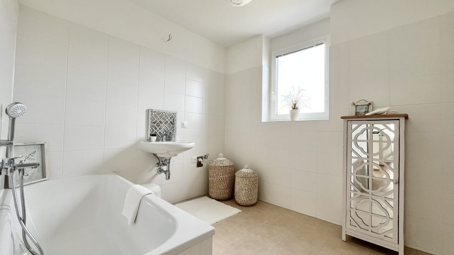 Modernes Badezimmer mit Badewanne, Waschbecken und dekorativem Schrank unter einem Fenster.