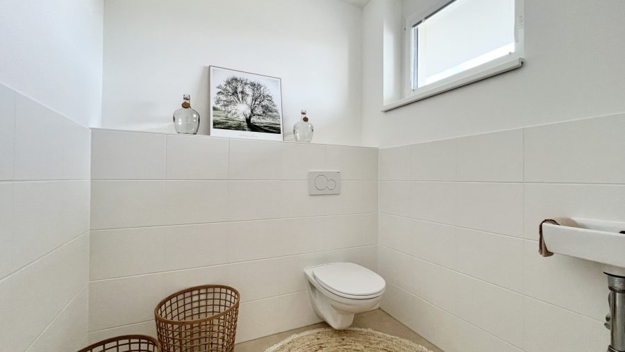 Modernes, weiß gefliestes Badezimmer mit hängendem WC, Deko und Fenster.