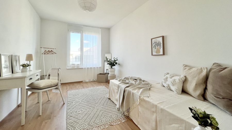 Helles, modern eingerichtetes Zimmer mit Sofa, Schreibtisch und Pflanzen, minimalistisch dekoriert.