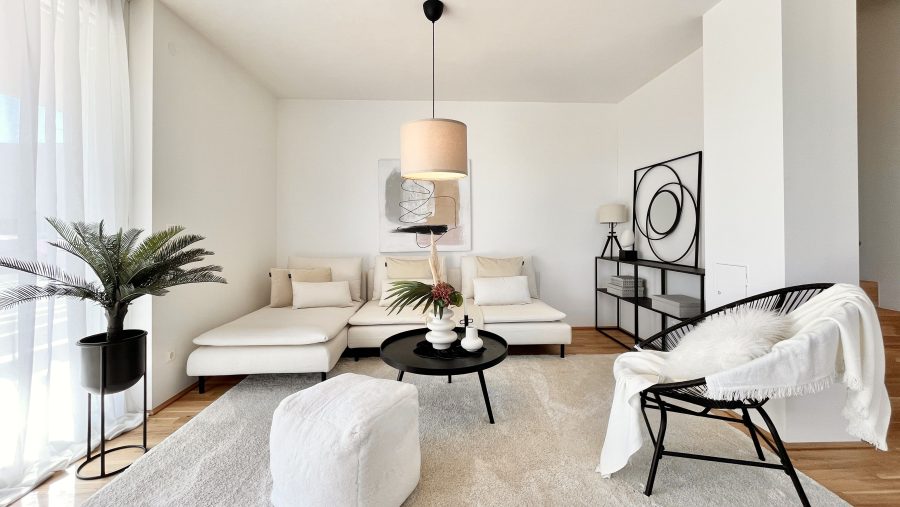 Modernes Wohnzimmer mit weißem Sofa, Couchtisch, Pflanzen und minimalistischer Dekoration.