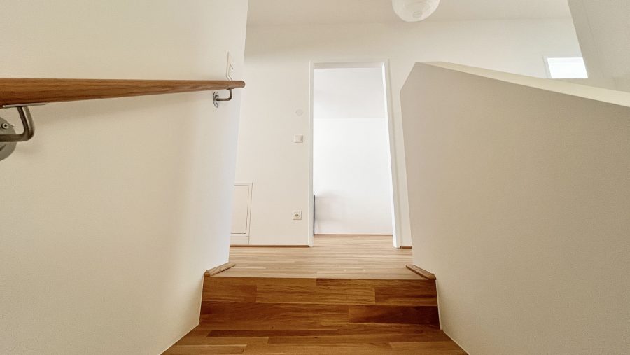 Treppe aus Holz in einem modernen, hellen Innenraum mit weißen Wänden und minimalistischem Design.