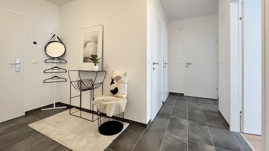 Moderner Flur mit Spiegel, Tisch und Pflanze auf grauen Fliesen, minimalistisch gestaltet.