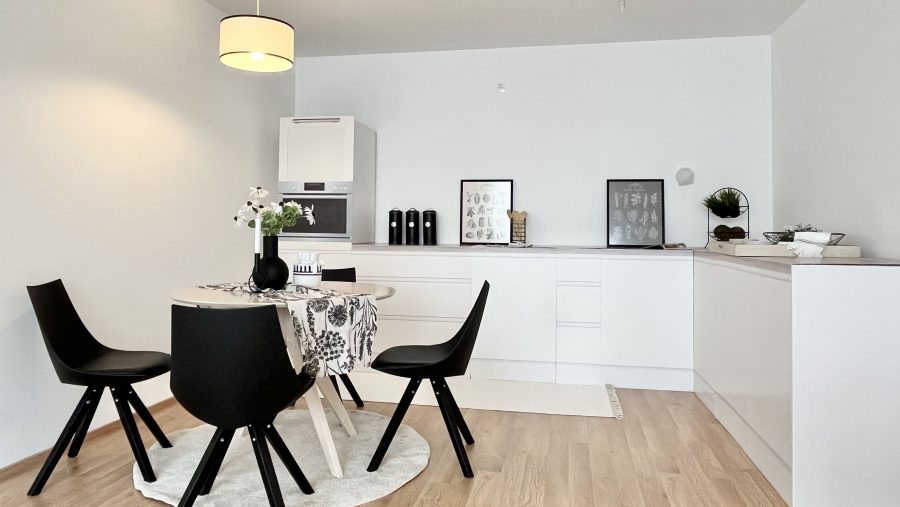 Moderne Küche mit Esstisch, schwarzen Stühlen und weißen Wänden, dekoriert mit Blumen und Bildern.