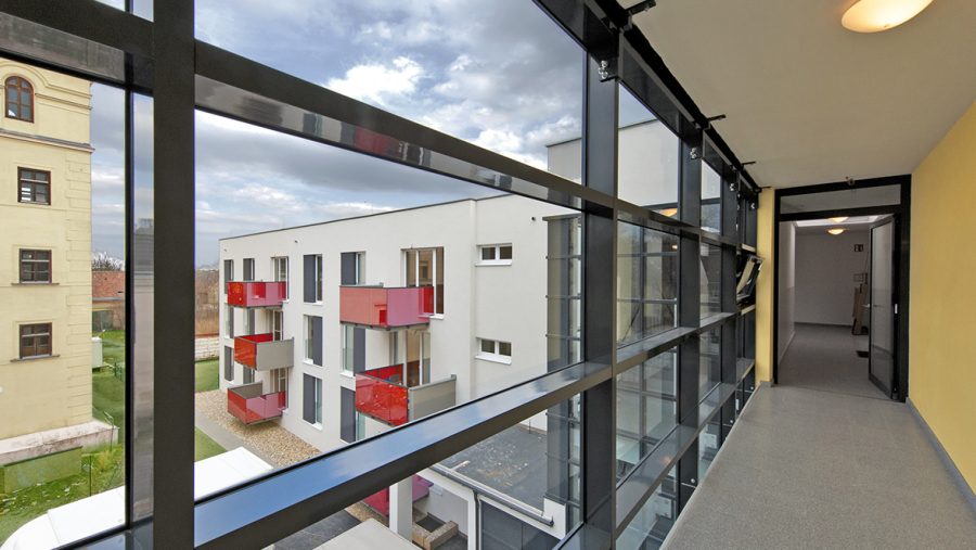 Moderner Wohnkomplex mit roten Balkonen, Blick von Innenbereich mit Fensterfront.