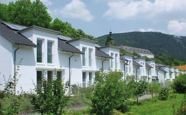 Reihenhäuser mit Solarpanelen in einer grünen Umgebung vor einem Hügel.