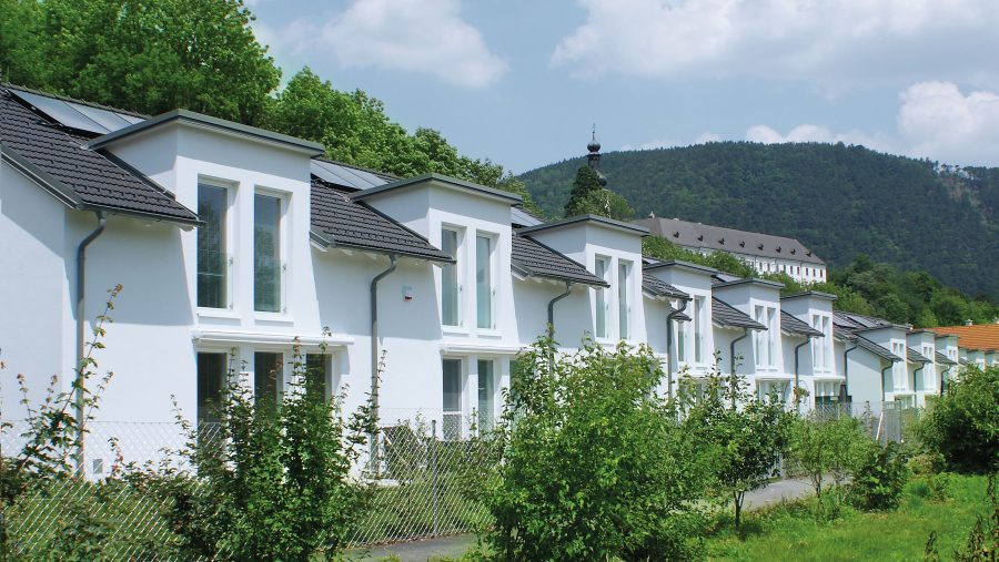 Reihenhäuser mit Solarpanelen in einer grünen Umgebung vor einem Hügel.