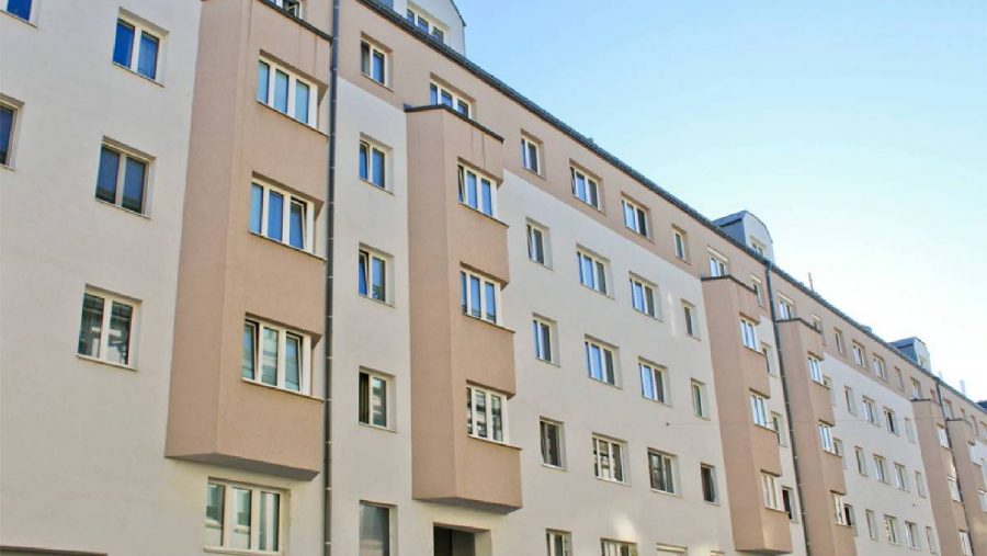 Mehrstöckiges Wohngebäude mit beige und weißen Fassaden unter klarem Himmel.