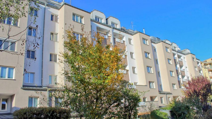 Mehrstöckiges Wohnhaus mit Bäumen im Vordergrund an einem sonnigen Tag.