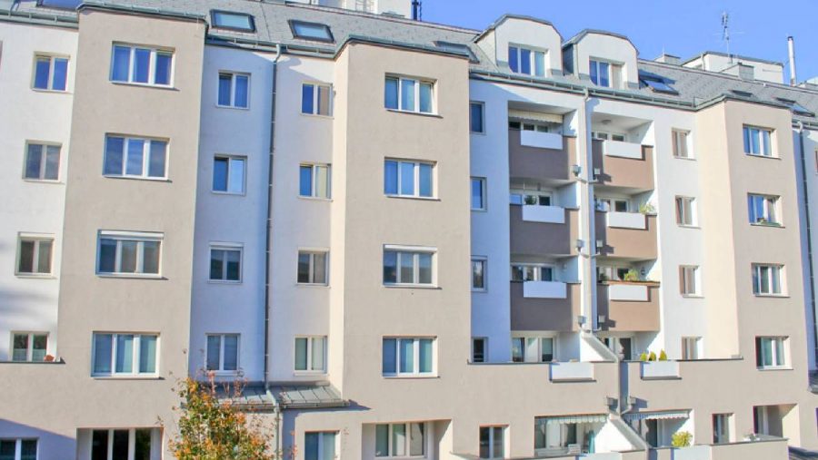 Mehrfamilienhaus mit Balkonen und Fenstern an einem sonnigen Tag.