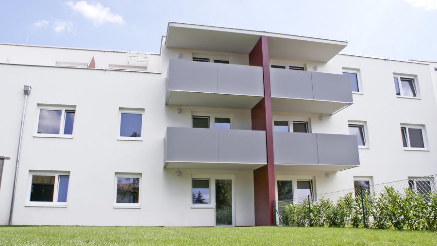 Moderne Mehrfamilienhausfassade mit Balkonen und gepflegtem Rasen im Vordergrund.