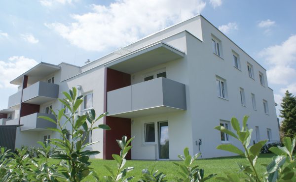 Moderne Wohnanlage mit Balkonen und grüner Umgebung unter blauem Himmel.