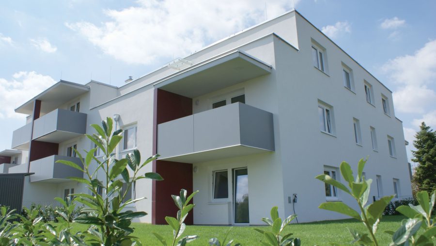 Moderne Wohnanlage mit Balkonen und grüner Umgebung unter blauem Himmel.